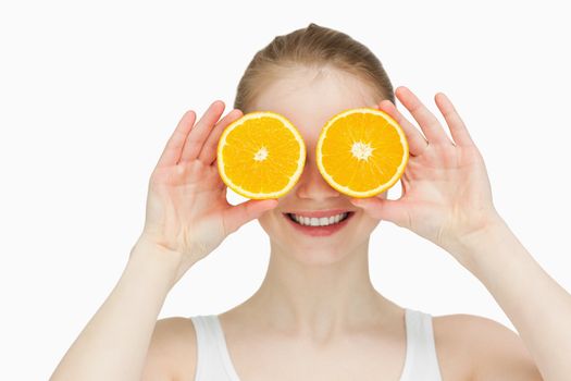 Smiling woman placing oranges on her eyes against white bakground