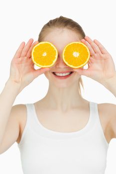 Cheerful woman placing oranges on her eyes against white background