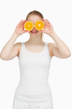 Joyful woman placing oranges on her eyes against white background