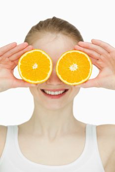 Close up of a woman placing oranges on her eyes against white background