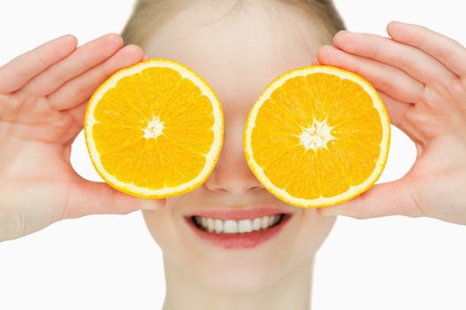 Close up of a cheerful woman placing oranges on her eyes against white background