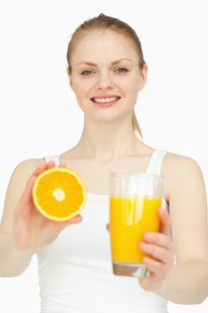 Smiling woman holding a glass while presenting an orange against white background