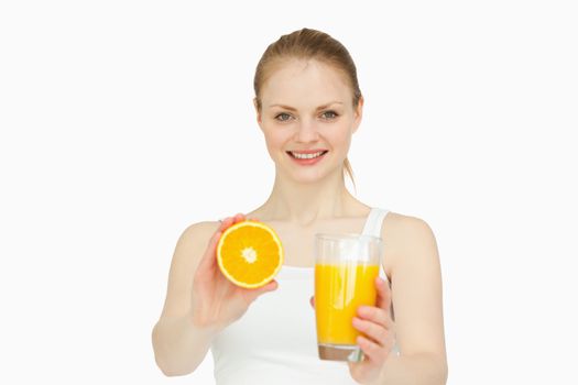 Cheerful woman presenting an orange while holding a glass against white background