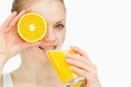 Woman placing an orange on her eye while drinking against white background