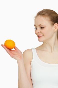 Smiling woman presenting a tangerine while looking at it against white background