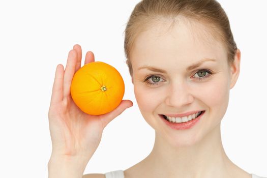Joyful blonde-haired presenting an orange against white background
