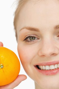 Close up of a cheerful woman holding an orange against white background