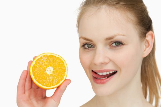 Woman holding an orange while placing her tongue on her lips against white background