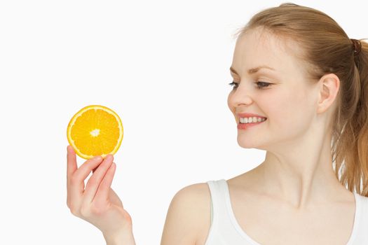 Woman presenting an orange slice while looking at it against white bakground