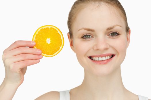 Cheerful woman holding a slice of orange against white background