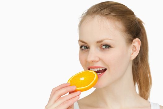 Woman placing an orange slice in her mouth against white background