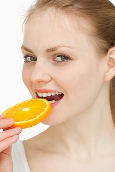 Close up of a woman placing an orange slice in her mouth against white background