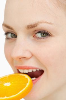 Close up of a woman placing a slice of orange in her mouth against white background