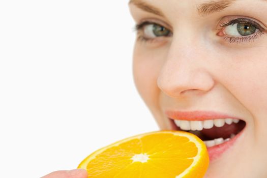 Close up of a woman placing a slice of an orange in her mouth against white background