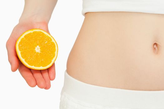 Woman placing an orange near her belly against white background