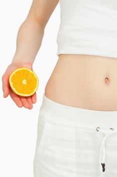 Close up of a woman placing an orange near her belly against white background