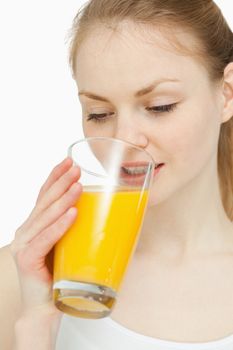 Woman drinking a glass of orange juice while looking at it against white background