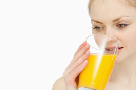 Woman drinking a glass of orange juice while looking away against white background