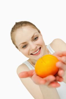 Cheerful woman holding a tangerine while looking at it against white background