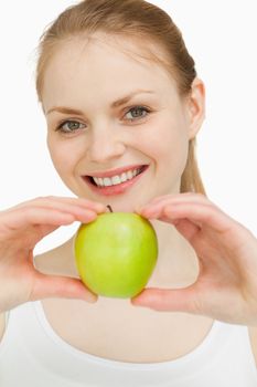 Blonde-haired girl smiling while presenting an apple against white background