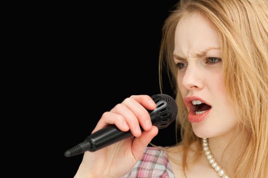 Woman singing while frowning against black background