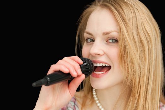 Young blond-haired woman singing against black background