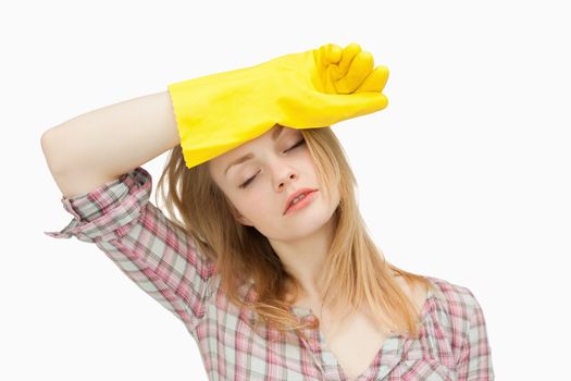 Woman wearing cleaning gloves while wiping her brow against white background