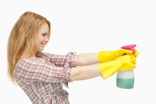 Fair-haired woman holding a spray bottle while smiling against white background