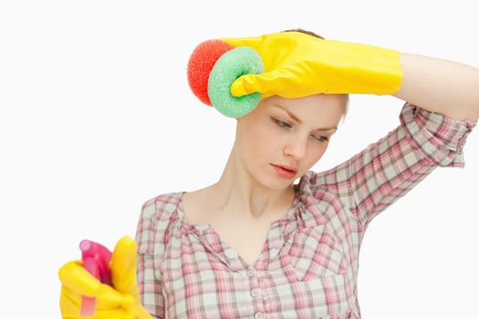 Young woman wiping her forehead while holding sponges against white background
