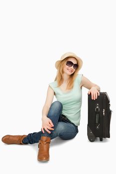 Blonde-haired woman sitting near a suitcase against white background