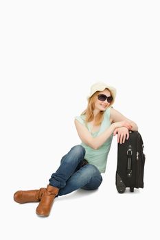 Woman smiling while sitting near a suitcase against white background