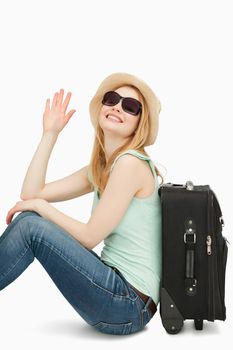 Woman sainsing her hand while sitting near a suitcase against white background