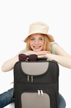 Woman leaning on a suitcase while sitting against white background
