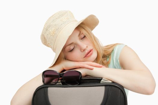 Woman asleep while leaning on a suitcase against white background