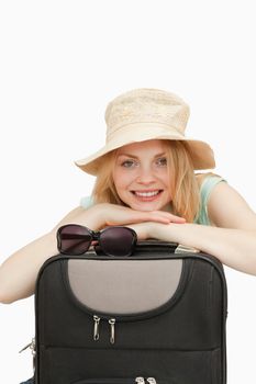 Smiling woman leaning on a suitcase against whitebackground