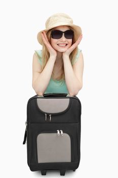 Cheerful woman leaning on a suitcase while sitting against white background