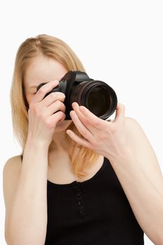 Young woman aiming with a camera against white background