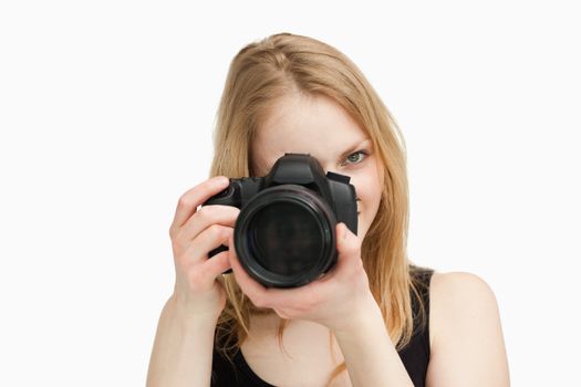 Fair-haired woman aiming with a camera against white background