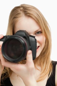 Blonde woman aiming with a camera against white background