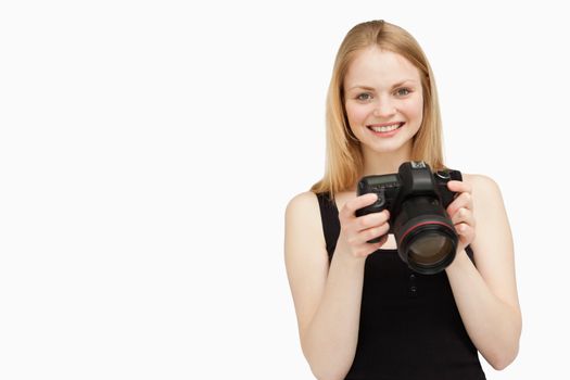 Woman holding a SLR camera while smiling against white background