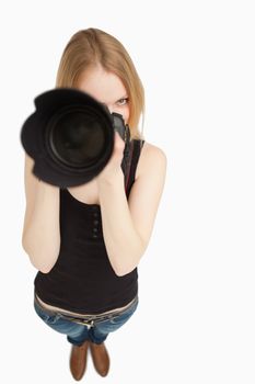 Blonde-haired girl aiming with her SLR camera against white background