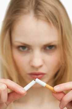 Close up of a serious woman breaking a cigarette against white background
