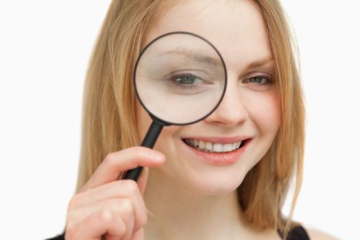 Woman placing a magnifying glass on her eye against white background