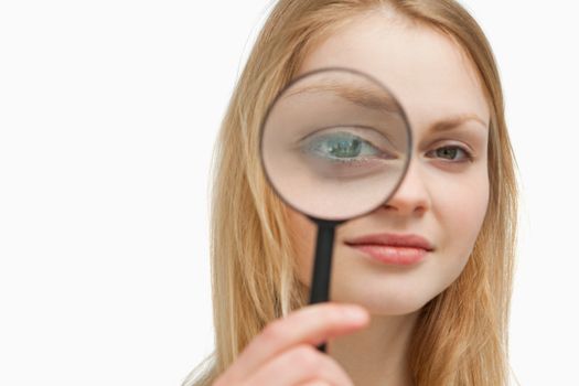 Close up of a woman placing a magnifying glass on her eyes against white background