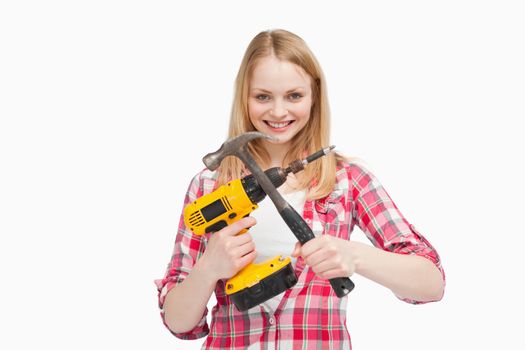Woman holding an electric screwdriver and a hammer against white background