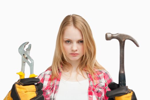 Serious woman holding a hammer and and a wrench against white background