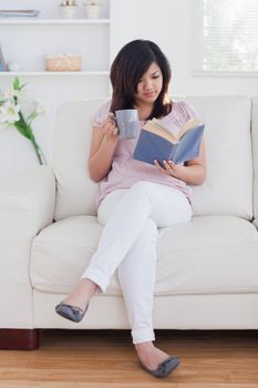 Woman reading a book while holding a mug on a sofa