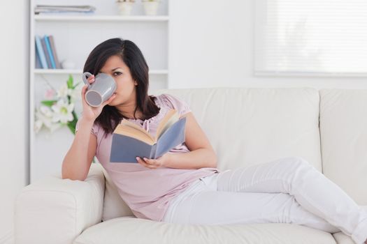 Woman drinking from a mug while lying on a sofa in a living room