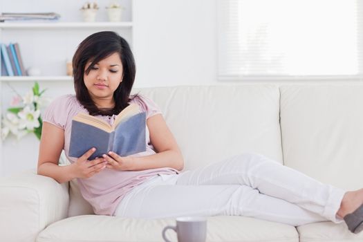 Woman reading a book while lying on a sofa in a living room