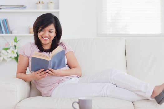 Woman reading a book while lying on a sofa in a living room